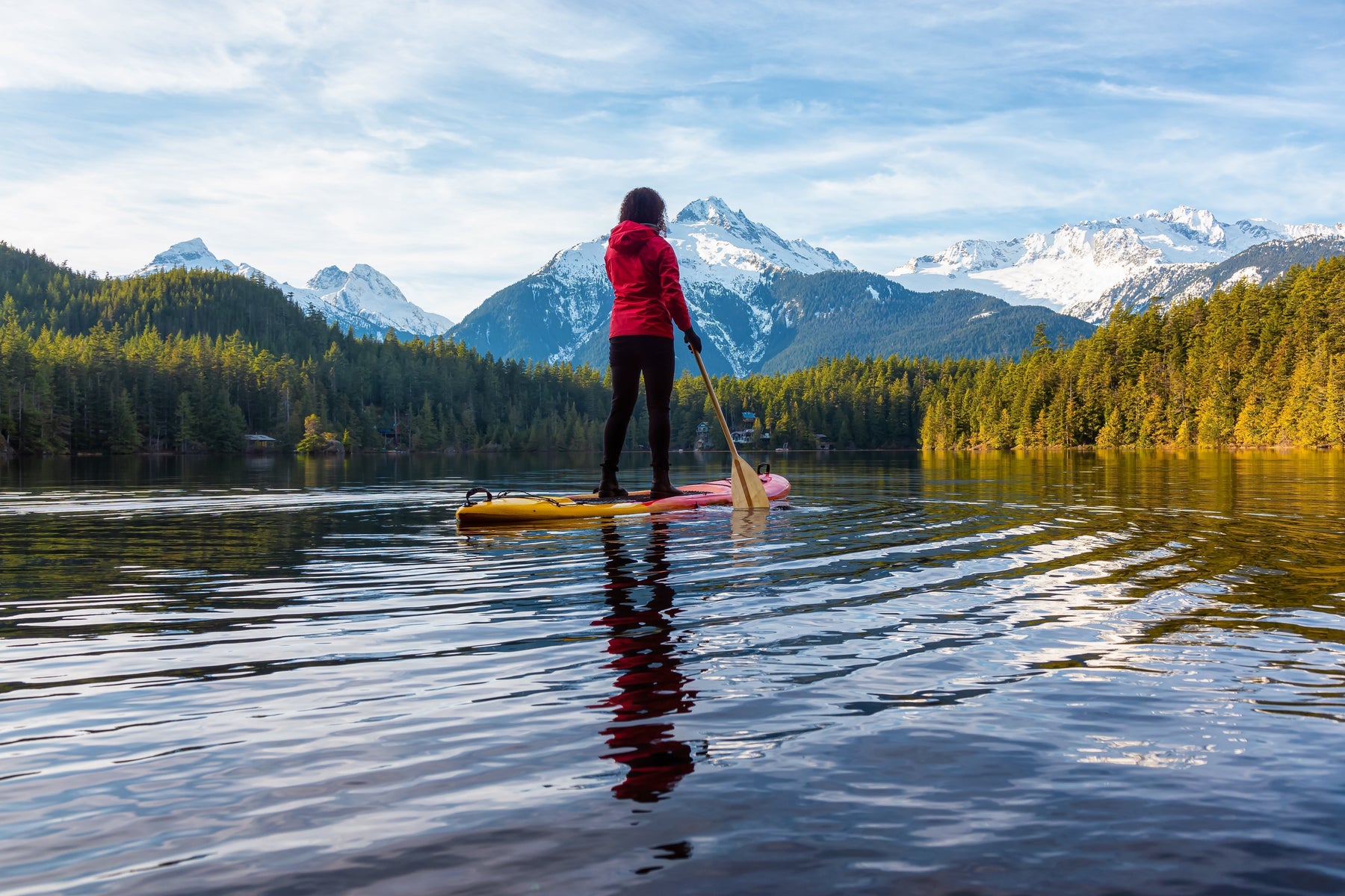 Woman paddle boarding on a mountain lake in Canada surrounded by snow-capped mountains.