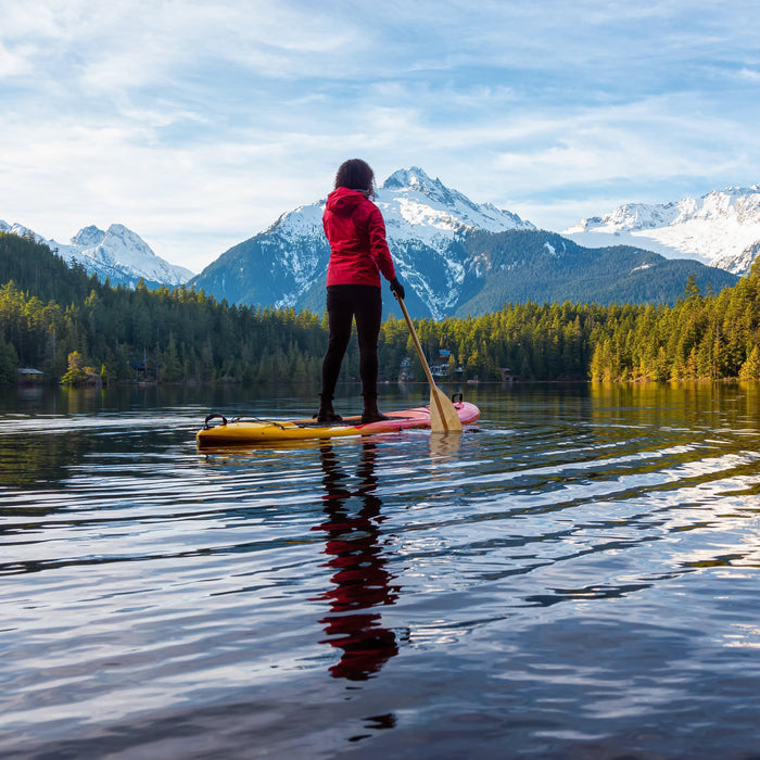 Woman paddle boarding on a mountain lake in Canada surrounded by snow-capped mountains.