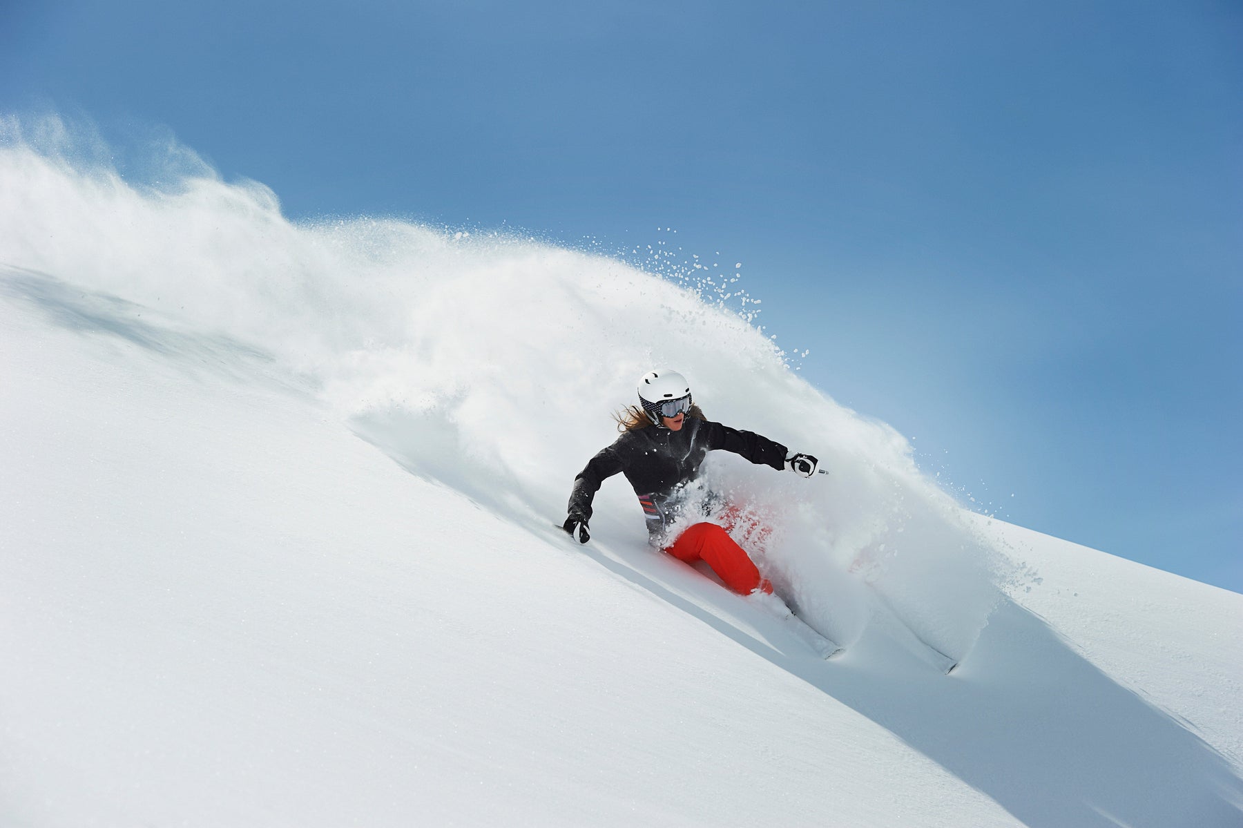 Woman skiing through fresh powder snow on a mountain slope.