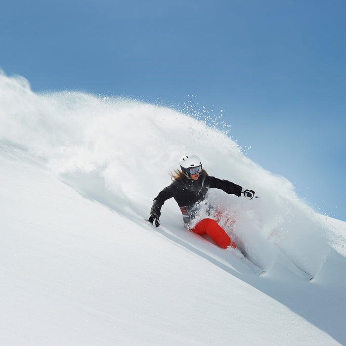 Woman skiing through fresh powder snow on a mountain slope.